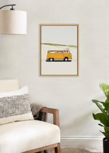 Framed illustration of a yellow vintage camper van with a small giraffe peeking out the roof hatch, set against a minimal background with a green hill.