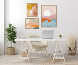 Minimalist white desk with beige chair in a bright room, featuring three abstract framed prints with warm sunrise colors and a green plant in a woven basket.