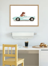 Framed illustration of a brown T. Rex dinosaur driving a light aqua 1957 Chevrolet Corvette, hanging above a child's desk with wooden chair and toys.