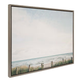Framed canvas showing a serene beach scene with pale blue sky, gentle waves, and a grassy sand dune behind a rope fence along the shore.
