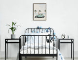 Minimalist bedroom with black metal bed frame, white bedding, pastel blue and gray string lights, small black side tables with plant, clock, and decor, and a framed vintage car and palm tree print on white wall.