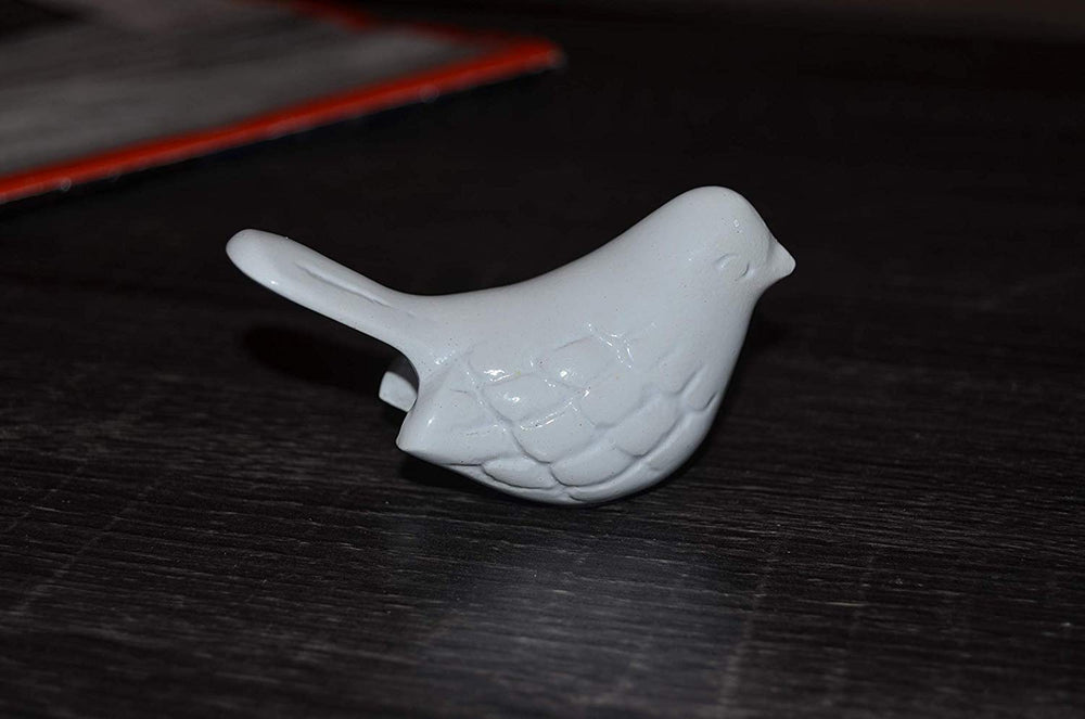 Small white ceramic bird figurine with textured wings and a slightly raised tail, placed on a dark wooden surface.