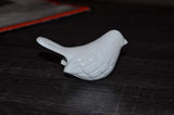 Small white ceramic bird figurine with textured wings and a slightly raised tail, placed on a dark wooden surface.