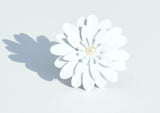 White floral napkin ring with layered petals and a central pearl-like bead casting a soft shadow on a white surface.