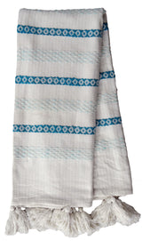 White handwoven throw with horizontal turquoise geometric patterned stripes and large white tassels on one end.