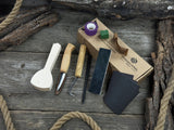 Beginner wood carving kit with sloyd knife, hook knife, wooden blank, sandpaper, sharpening board, pencil, and finger wrap
