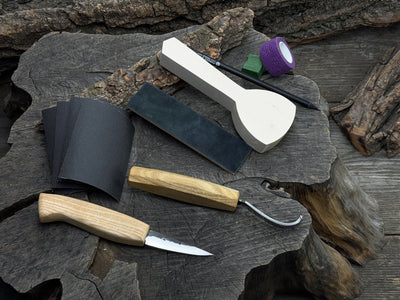 Beginner wood carving kit with sloyd knife, hook knife, wooden blank, sandpaper, sharpening board, pencil, and finger wrap