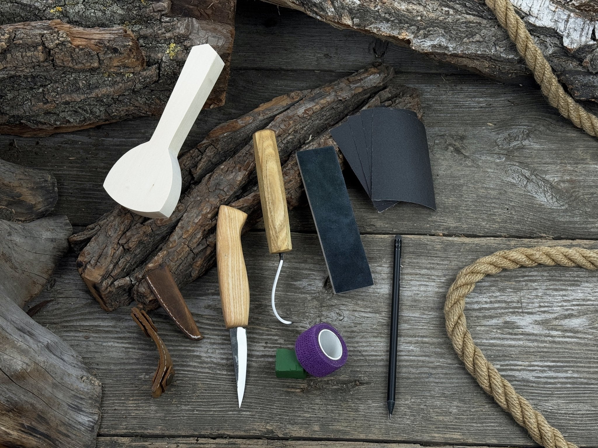 Beginner wood carving kit with sloyd knife, hook knife, wooden blank, sandpaper, sharpening board, pencil, and finger wrap