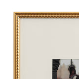 Close-up of a gold photo frame corner with a rounded bead pattern along the inner edge, surrounding a white mat and a partial photo with blurred background.