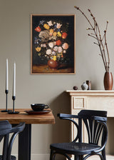 Still life painting of a colorful bouquet in a round earthenware vase, framed with a gold beaded edge, hanging on a beige wall above a fireplace.