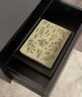 Light green journal with intricate darker green leaf and floral patterns inside a black drawer against a stone floor background