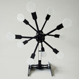 Black metal mechanical target with twelve arms radiating from a central hub, each arm ending in a round white disc, mounted on a foldable black stand.