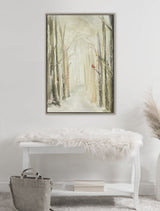 Framed canvas painting of a foggy winter forest with tall bare trees and a single red cardinal perched on a branch, hanging above a white bench with a fur throw.