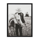 Black and white photo of a person wearing a hat and jacket gently holding the reins of a light-colored horse in a grassy field with blurred distant trees.