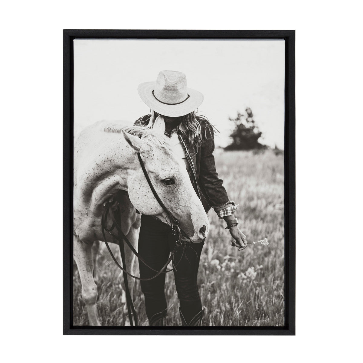 Black and white photo of a person wearing a hat and jacket gently holding the reins of a light-colored horse in a grassy field with blurred distant trees.