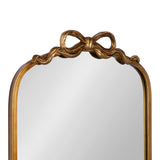 Arched mirror with a gold frame featuring a sculpted ribbon bow detail at the top center and softly curved edges.