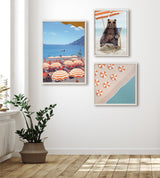 Three framed wall artworks showing a beach scene with orange-striped umbrellas, a bear wearing sunglasses lounging in a chair, and an aerial view of beach umbrellas by blue water.