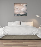 Sepia-toned framed canvas above a white bed with ruffled pillows, depicting clouds over a misty landscape in soft brown and gray hues.