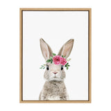 Frontal portrait of a gray and white bunny with upright ears wearing a pink rose and green leaf crown on a white background, framed in natural wood.