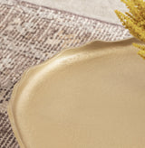 Close-up of a gold-toned table edge with a subtle scalloped design against a textured rug background and a yellow floral accent.