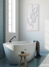 Modern white freestanding bathtub with black faucet on blue tiled floor, a wooden stool with bath items, and a framed minimalist blue botanical line art on white wall.