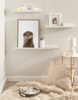 Framed canvas of a smiling otter with wet fur on a white floating shelf in a neutral-toned cozy corner with soft beige pillow, faux fur rug, and small round side table.