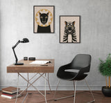 Minimalist office corner with wooden desk, black modern chair, and two animal portrait canvases—a stylized lion and tiger—on a light gray textured wall.