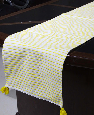 Cotton table runner with yellow and white stripes laid out on a wooden dining table