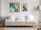 Living room with a white three-seat sofa centered on a wooden floor, featuring two colorful framed artworks on the wall and a tall floor lamp on the right.
