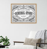 Black and white vintage-style framed print reading 'Family Owned & Operated General Store and Market' with decorative floral and scrollwork border, hanging above white armchair.