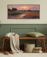 Softly lit landscape painting with a glowing sun over misty foothills and a reflective river, framed and hung above a wooden bench with a green pillow and draped blanket.