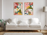 Two vertical floral canvas prints with pink, red, yellow, and green shades, framed in wood, hung side by side above a white three-seat sofa with cushions.