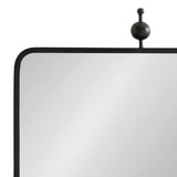 Close-up of a square mirror with a thin black metal frame, rounded corner, and a decorative black metal ball finial on top.