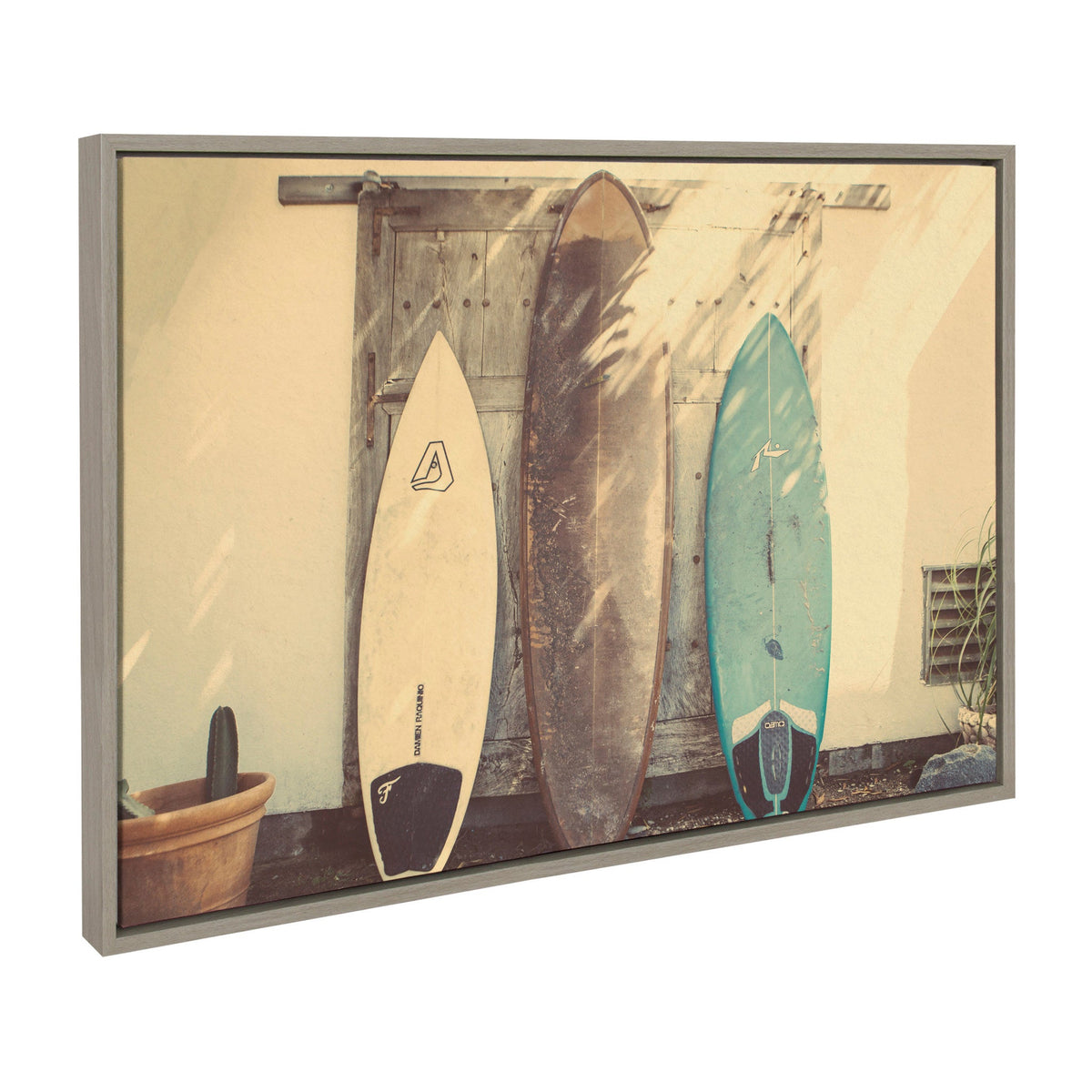 Three surfboards leaning against a weathered beige wall with a wooden door and a potted cactus on the left side, casting soft shadows.