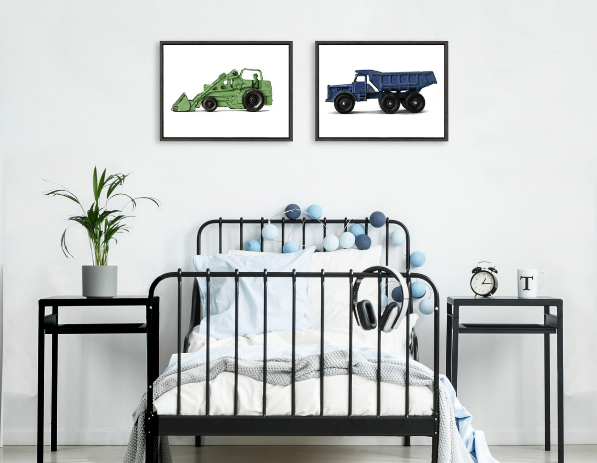 Two framed watercolor paintings above a black metal bed; left shows a green vintage toy tractor, right shows a blue vintage toy dump truck, both on white backgrounds.