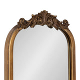 Arched mirror with an ornate, carved frame featuring scrollwork and leaf motifs in a warm gold finish above the glass.