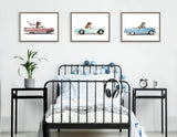 Three framed illustrations above a black metal bed frame; each shows a cartoon T Rex driving a pastel-colored 1957 Chevrolet convertible, in pink, aqua, and blue.