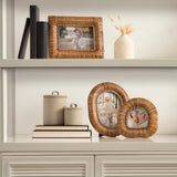 Two rounded rattan tabletop picture frames with photos, placed on a white shelf alongside beige ceramic canisters and stacked books, with a woven rattan frame and decorative vase above.