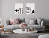 Two black and white framed prints featuring retro Art Deco Miami Beach architecture with palm trees, hung above a light gray sofa with textured pink and gray pillows.