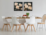 Dining area with a wooden-top white table surrounded by four white modern chairs and one wooden chair, beneath two framed floral canvas artworks with pale pink flowers on black backgrounds.