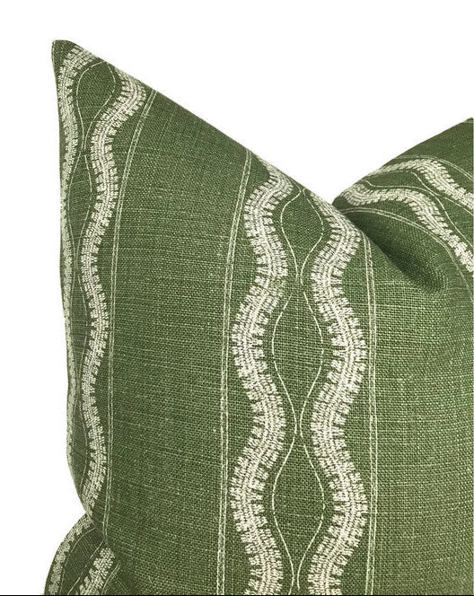 Green fabric pillow cover with vertical white wavy line patterns and subtle horizontal thread texture, showing a close-up of a corner and part of the front panel.