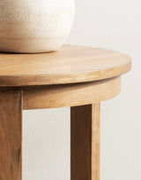 Close-up of a round wooden side table with a smooth light wood top and matching legs, showing natural wood grain and a beige ceramic vase partially visible on top.