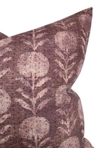 Close-up of a berry-colored pillow with a faded botanical pattern featuring round floral shapes and leafy stems on textured fabric.