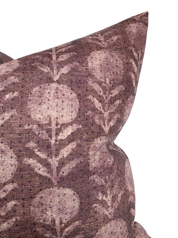 Close-up of a berry-colored pillow with a faded botanical pattern featuring round floral shapes and leafy stems on textured fabric.