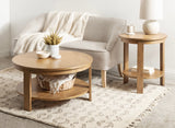 Light wood round coffee table and side table with lower shelves on a beige patterned rug, next to a light beige upholstered chair with a blanket.