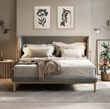 Bedroom with a gray upholstered bed featuring layered beige and cream pillows, a textured throw blanket, two botanical framed canvases in black and white above the headboard, and pendant lamps on either side.