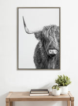Black and white close-up portrait of a Highland cow with long shaggy hair partially covering its eyes and a single visible curved horn in a thin dark frame.
