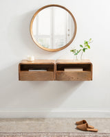 Pair of floating wooden shelves with drawers mounted on a white wall, topped with a candle and a small glass vase with green plant cuttings, beneath a round wooden-framed mirror.