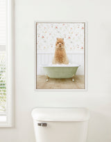 Framed canvas print of a curly golden alpaca sitting in a green cast-iron bathtub filled with bubbles, against floral wallpaper in a country cottage style bathroom.