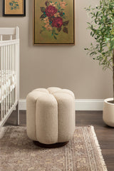 Cream-colored round tufted ottoman with a plush textured fabric and dark wooden base, placed on a patterned rug beside a white crib and a potted plant.